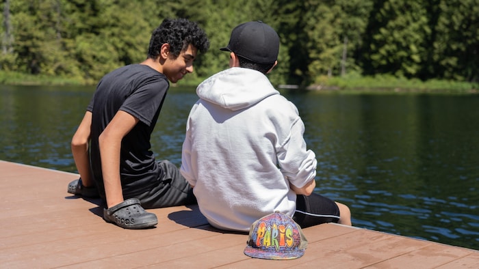 Deux jeunes sont assis au bord d'un lac et discutent.