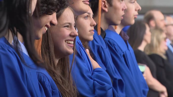 Une jeune diplômée souriante dans une rangée d'élèves debout.