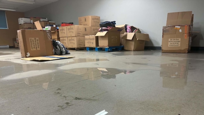 De l'eau s'accumule sur le plancher du sous-sol où sont entassées des boîtes de carton remplies de matériel scolaire.