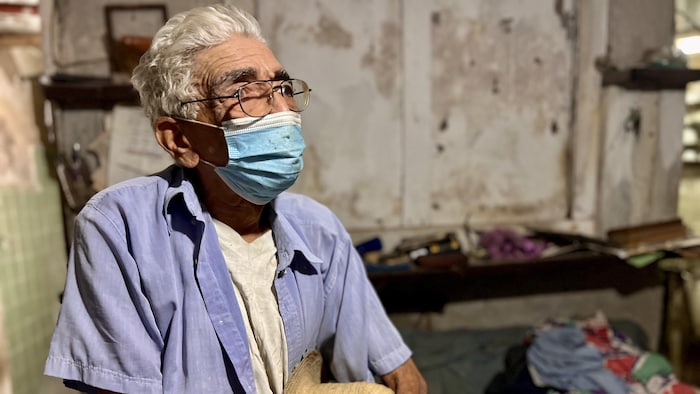 Un homme porte un masque et tient un chapeau. 