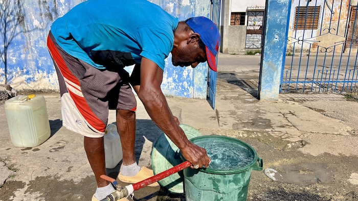 Un homme remplit une poubelle de plastique d'eau. 