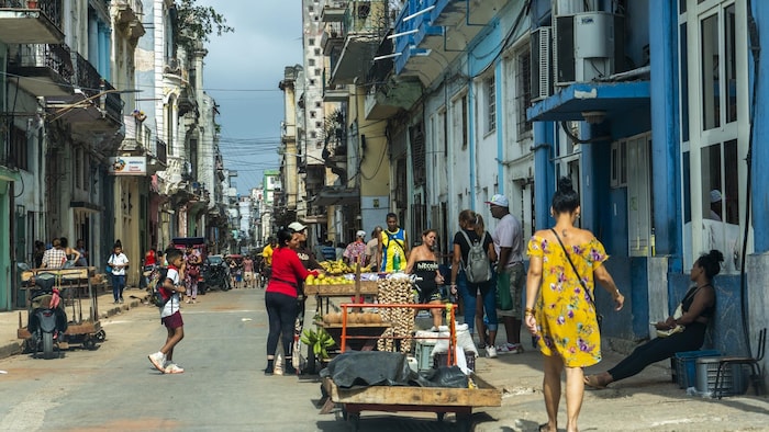 Des gens marchent dans la rue et un petit kiosque de fruits est installé. 
