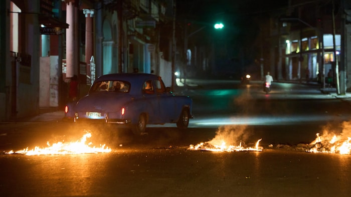 Une vieille voiture passe derrière du feu dans une rue de La Havane. 