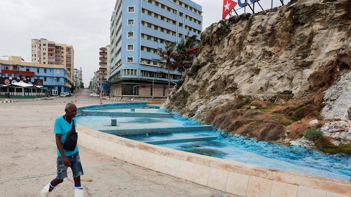 Un homme marche devant une fontaine vide.