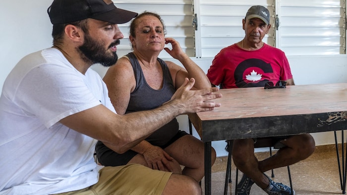Un jeune homme et ses deux parents assis à une table.

