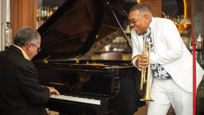 Un homme au piano et un homme appuyé sur le piano avec une trompette à la main.