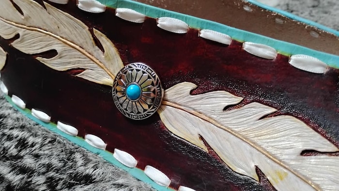Une large ceinture avec deux plumes découpées dans le cuir.