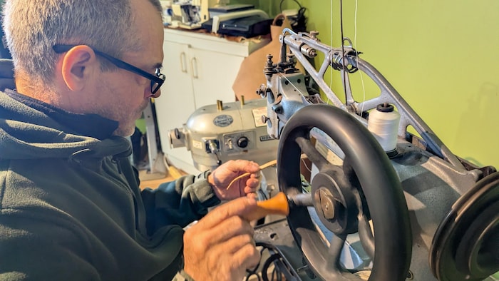L'artisan utilise une vieille machine à coudre avec une roulette pour coudre un fil sur un bout de cuir. 