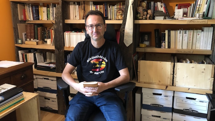 Charles Sagalane est assis dans sa bibliothèque.