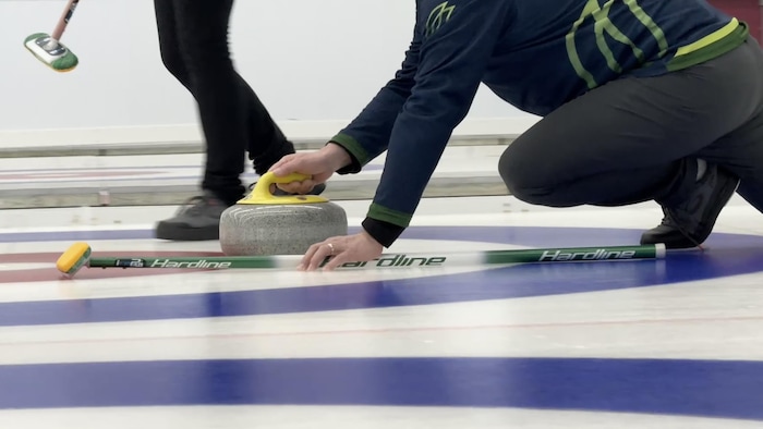 Un joueur de curling stabilise sa pierre sur la glace lors du tournoi Manicouagan Invitation au Pavillon du Lac.