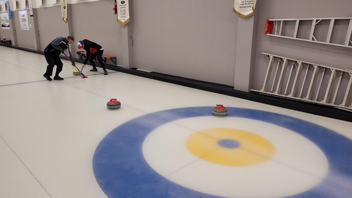 Des joueurs de curling frottent leur balai sur la glace pour faire avancer une pierre.
