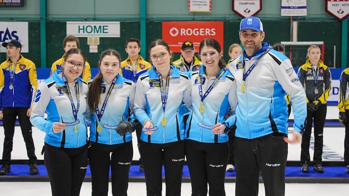 Quatre jeunes filles avec leur entraineur qui ont une médaille d'or au cou.