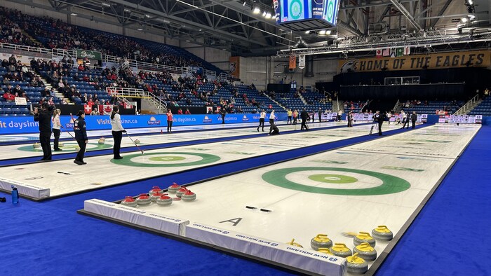 Des gens regardent des joueuses de curling sur la glace.