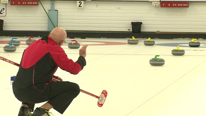 Un joueur de curling analyse la disposition des pierres sur la glace.
