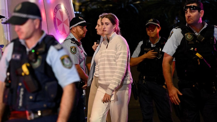 Une jeune femme marche, escortée par des policiers.