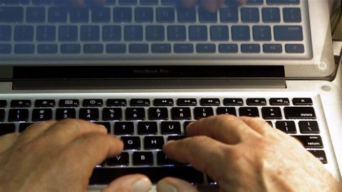 Des mains d'homme tapent sur un clavier d'ordinateur portable.