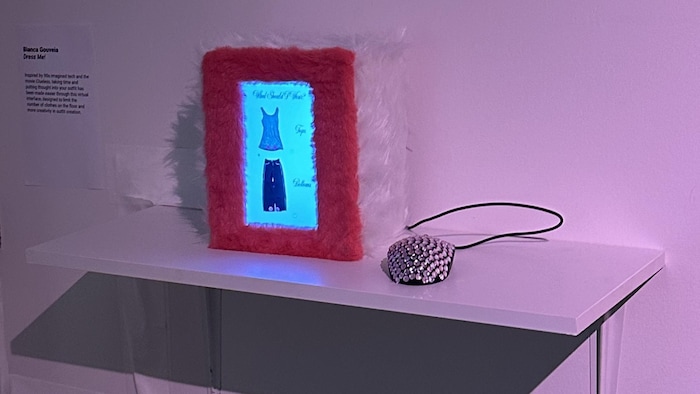 Un écran entouré d'une fausse fourrure est posé sur un présentoir. Le cyberdeck est relié à une souris d'ordinateur recouverte de paillettes.
