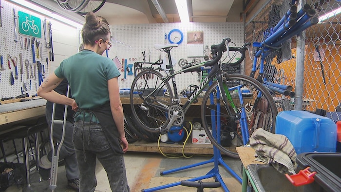Deux personnes regardent un vélo accroché dans un atelier de réparation. 