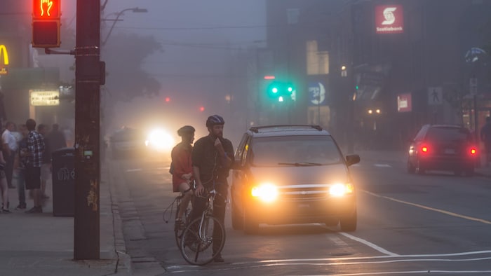 Des piétons, des cyclistes et des voitures par une journée sombre et pluvieuse.