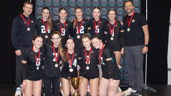 Une équipe de volleyball avec des médailles au cou et un trophée pose pour une photo.