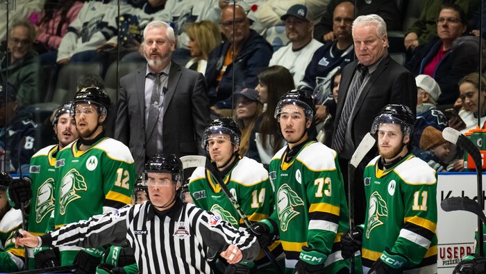 Un entraîneur derrière le banc avec des joueurs. 