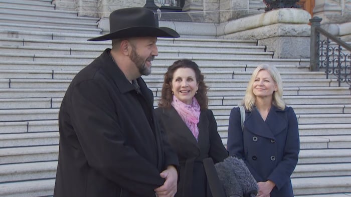 Trois personnes devant les escaliers de la façade de l'Assemblée législative de la Colombie-Britannique. 