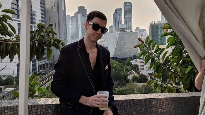 Dallas Pokornik assis sur la balustrade d'un immeuble avec un verre à la main