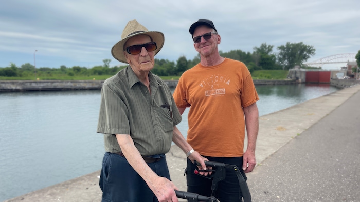 Deux hommes sourient à la caméra debout sur le chemin pédestre en bordure de la rivière St Mary’s.