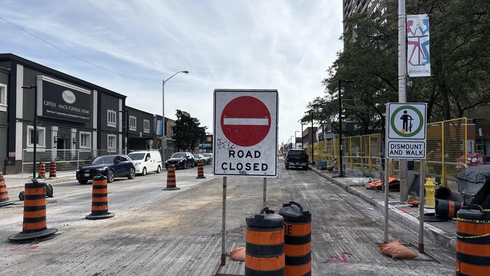 Un chantier sur l'avenue Danforth avec des cônes, des barrières et un panneau indiquant que la route est fermée.
