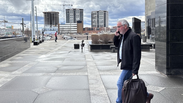 Un homme aux cheveux gris sort du palais de justice de Moncton. Il a un téléphone cellulaire à l'oreille.