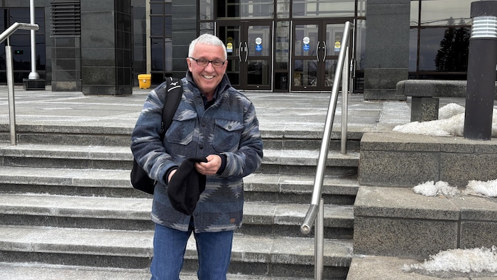 Un homme souriant regarde la caméra devant le palais de justice de Moncton.