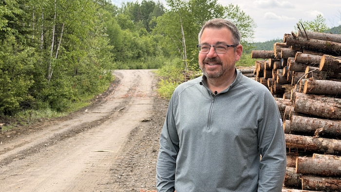 Un homme devant une pile de bois sourit à la caméra.