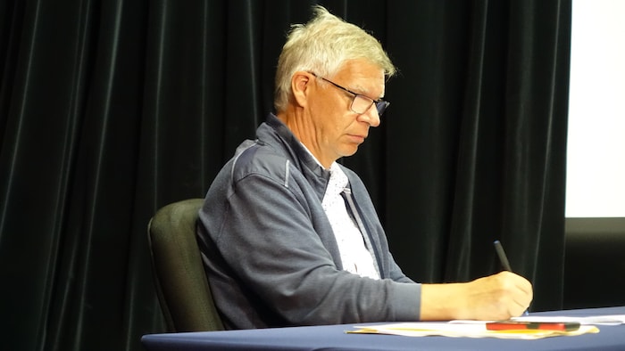 Homme prenant des notes en position assise, sur une table.