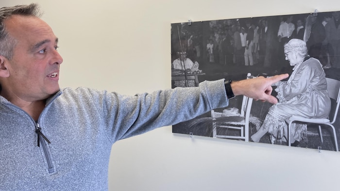 Un homme pointe une photo d'archives exposée sur un mur.