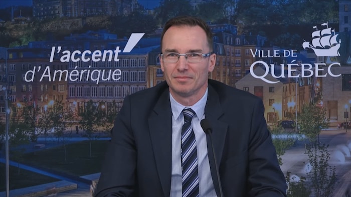 Un homme portant veston et cravate lors d'une conférence de presse à l'hôtel de ville de Québec.