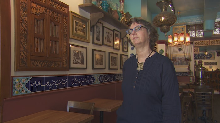 Une femme portant des lunettes dans un restaurant vide avec des décorations et des tuiles de style iranien.