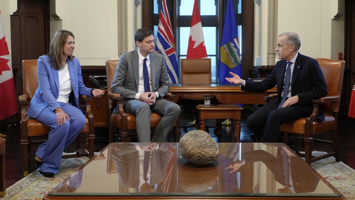 Danielle Smith, David Eby et Mark Carney discutent assis.