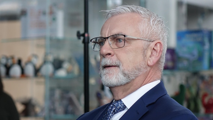 Un homme de profil, portant des lunettes et une courte barbe blanche, regarde vers la gauche de l'image d'un air concentré.