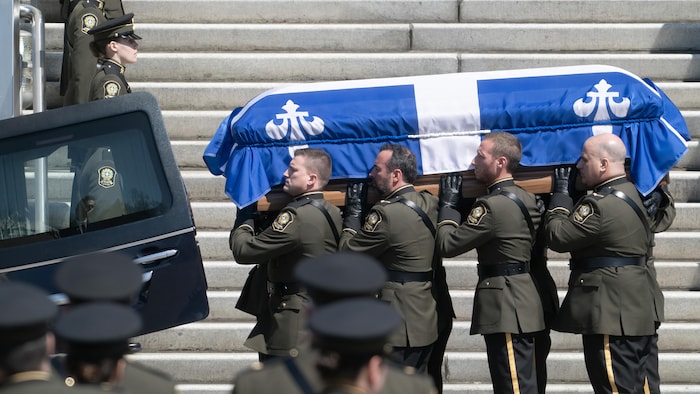 Des agents de la Sûreté du Québec portent un cercueil.