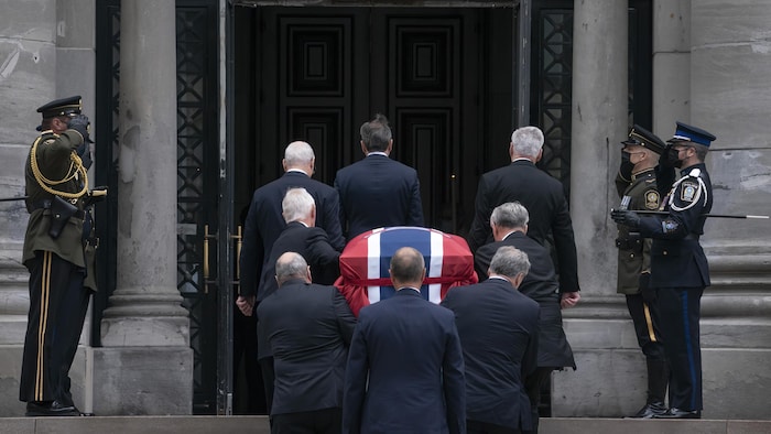 Des porteurs font entrer dans l'église un cercueil recouvert d'un drapeau du Canadien de Montréal.