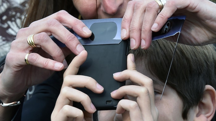 Une femme et un enfant utilisent un téléphone et des lunettes de protection pour photographier une éclipse.