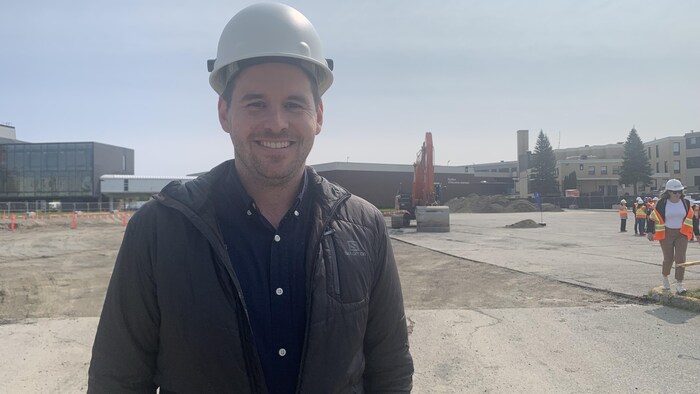 Un homme en casque de protection dans un chantier sourit à la caméra.
