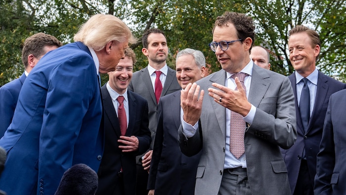 Dario Amodei a les deux mains ouvertes devant lui pendant qu'il parle. Donald Trump s'incline en sa direction. Mark Zuckerberg est derrière et éclate de rire.