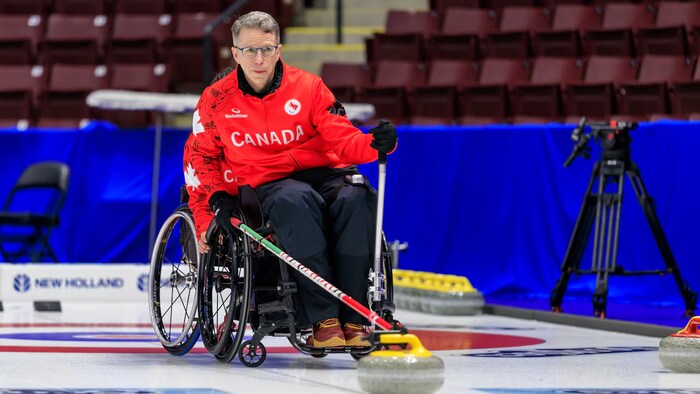 Gilbert Dash s'apprête à relâcher la pierre de curling, sur la glace.