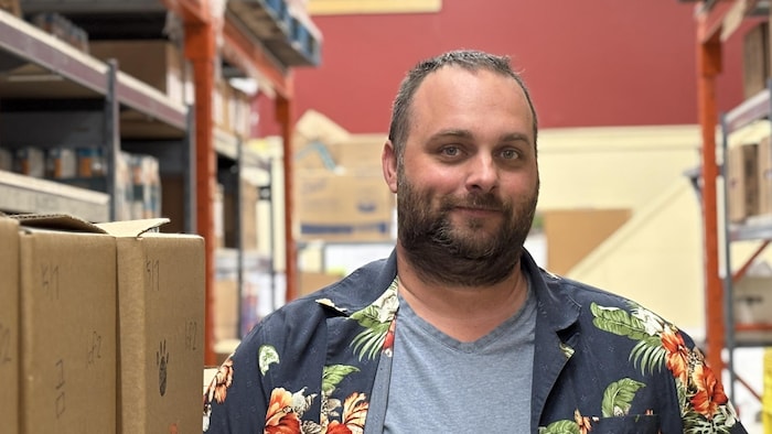 Portrait de Dave Blottner à la banque alimentaire, entre des boîtes de denrées destinées aux communautés en dehors de Whitehorse.