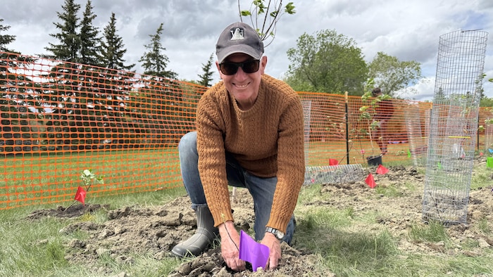Dave Hall sourit à la caméra en semant une plante.