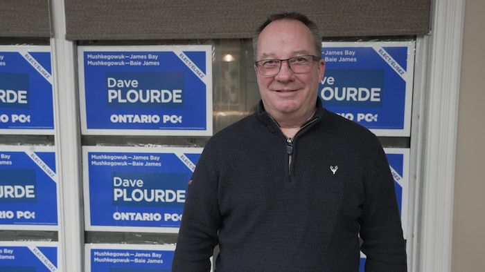 Dave Plourde devant un mur de pancartes pour sa campagne.