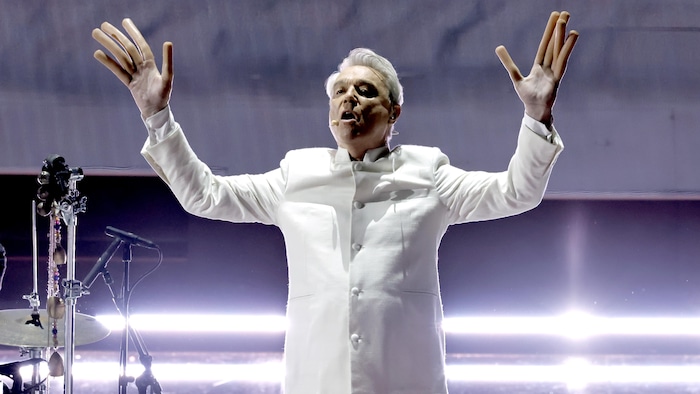 David Byrne, les mains dans les airs avec des doigts-saucisses, sur scène.