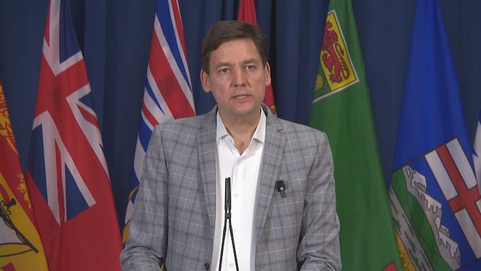 David Eby devant des drapeaux de plusieurs provinces canadiennes.