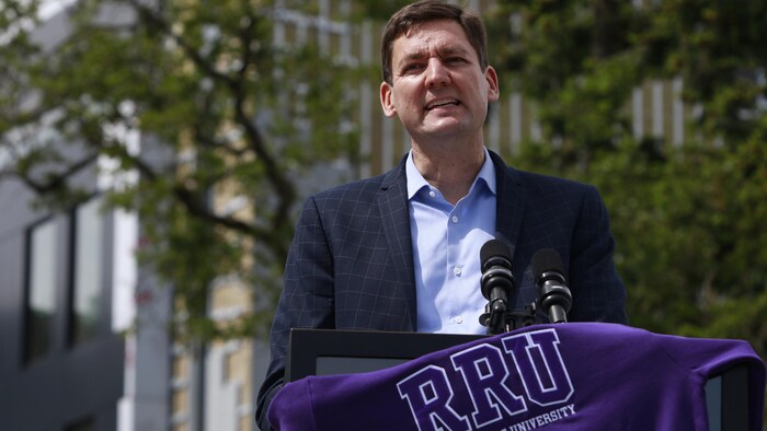 Le premier ministre David Eby devant un podium, avec des arbres en arrière-plan.